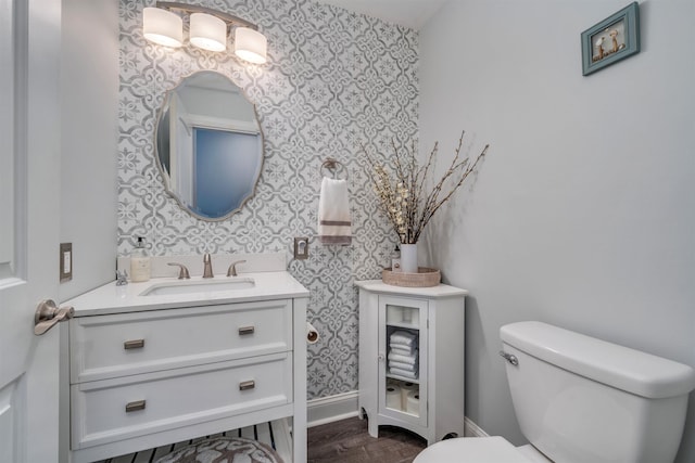 half bath with wallpapered walls, baseboards, toilet, wood finished floors, and vanity