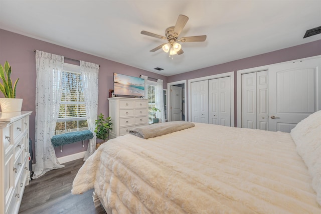 bedroom featuring a ceiling fan, dark wood-style flooring, visible vents, and multiple closets