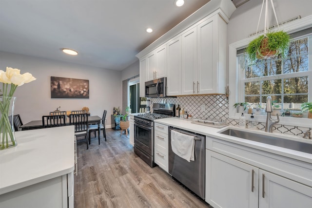 kitchen with tasteful backsplash, stainless steel appliances, light countertops, white cabinetry, and a sink