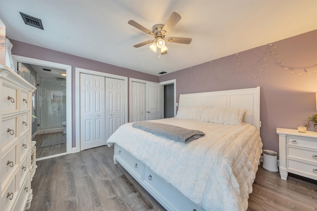 bedroom with ceiling fan, visible vents, multiple closets, dark wood-style floors, and ensuite bath