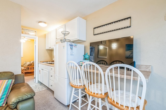 kitchen with light carpet, white refrigerator, white cabinetry, and ceiling fan