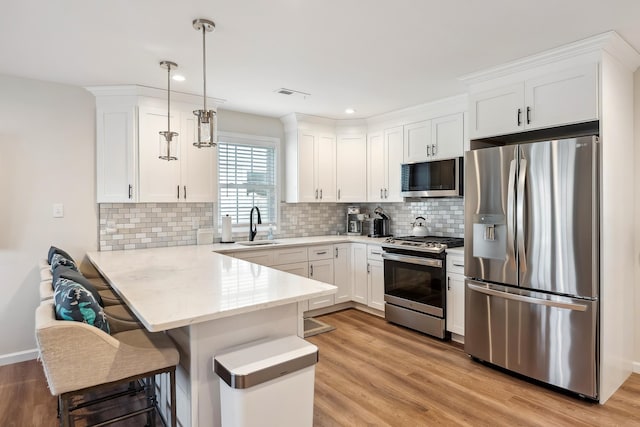 kitchen with white cabinets, visible vents, a peninsula, appliances with stainless steel finishes, and a sink