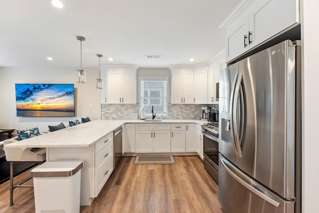 kitchen with white cabinets, a peninsula, a kitchen bar, stainless steel appliances, and a sink
