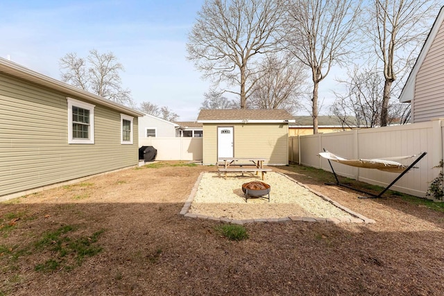 back of property featuring a fire pit, a fenced backyard, and an outdoor structure