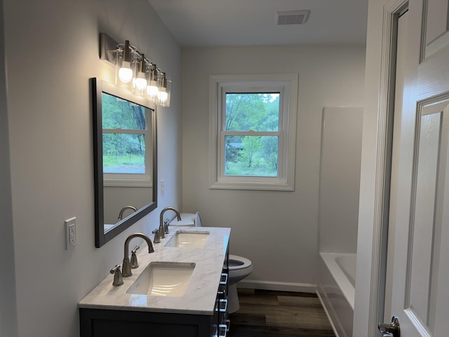 full bath with toilet, wood finished floors, a tub to relax in, double vanity, and baseboards