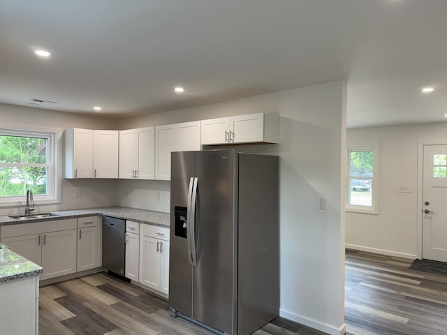 kitchen with appliances with stainless steel finishes, a sink, dark wood-type flooring, light stone counters, and white cabinetry