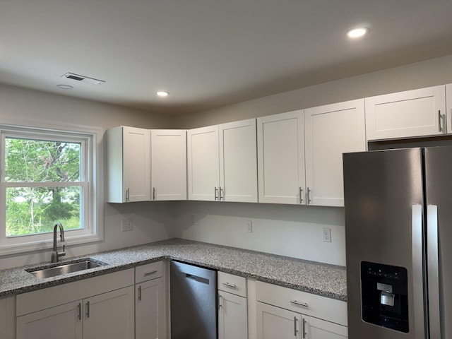 kitchen featuring appliances with stainless steel finishes, a sink, recessed lighting, white cabinets, and light stone counters