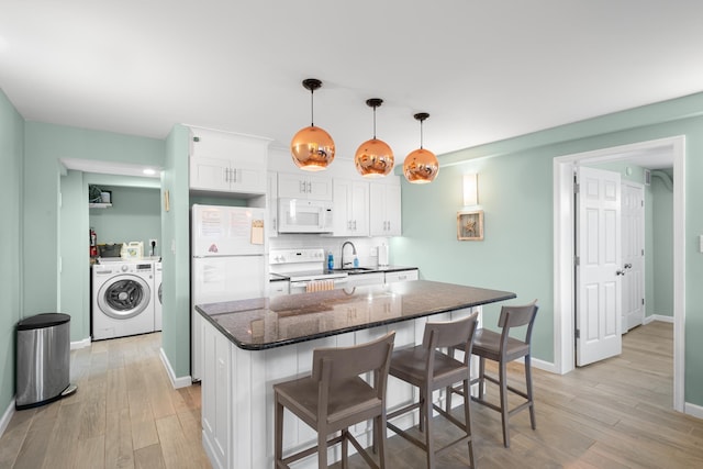 kitchen with washer and dryer, a breakfast bar, white cabinets, hanging light fixtures, and white appliances