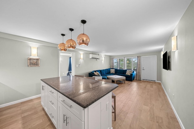 kitchen with a kitchen bar, an AC wall unit, a kitchen island, dark stone counters, and white cabinets