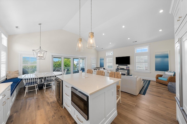 kitchen featuring built in microwave, white cabinetry, a center island, lofted ceiling, and decorative light fixtures