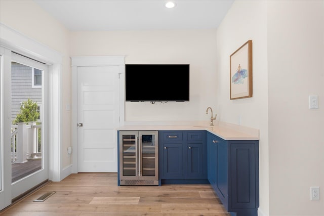 bar with blue cabinetry, light hardwood / wood-style flooring, wine cooler, and a healthy amount of sunlight