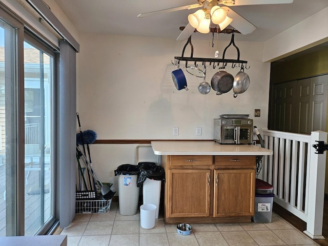 kitchen with light countertops, brown cabinetry, a ceiling fan, and light tile patterned flooring