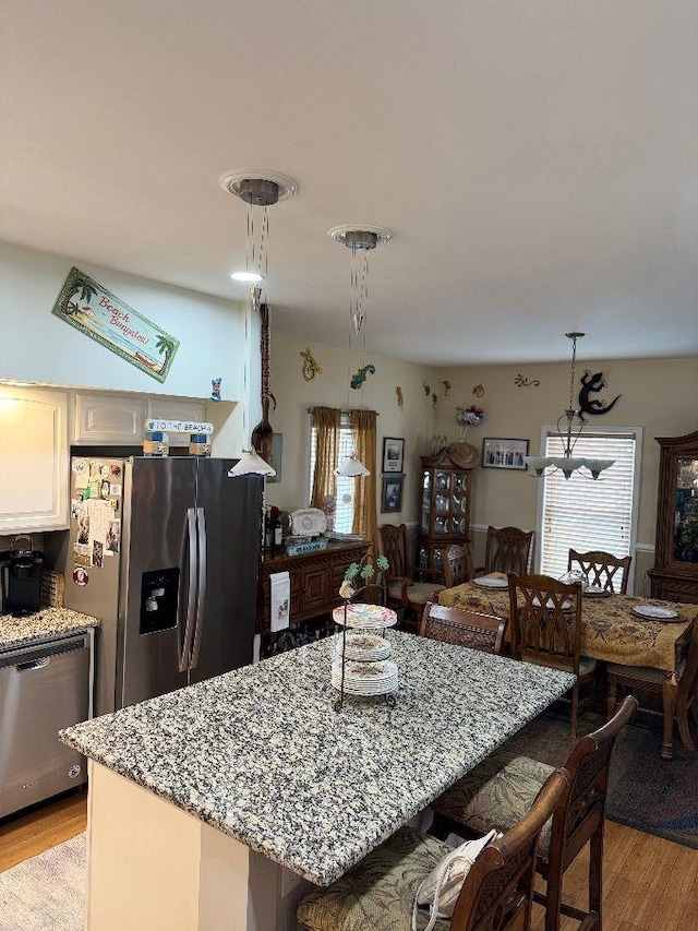 kitchen with appliances with stainless steel finishes, light hardwood / wood-style flooring, pendant lighting, and light stone counters