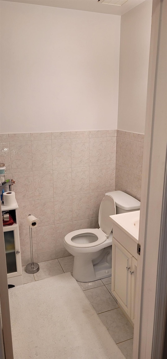 bathroom with toilet, vanity, tile patterned floors, and tile walls