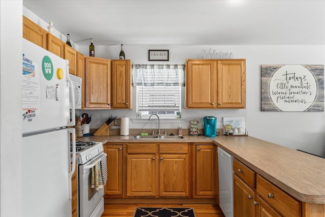 kitchen featuring white appliances, brown cabinetry, a peninsula, and a sink