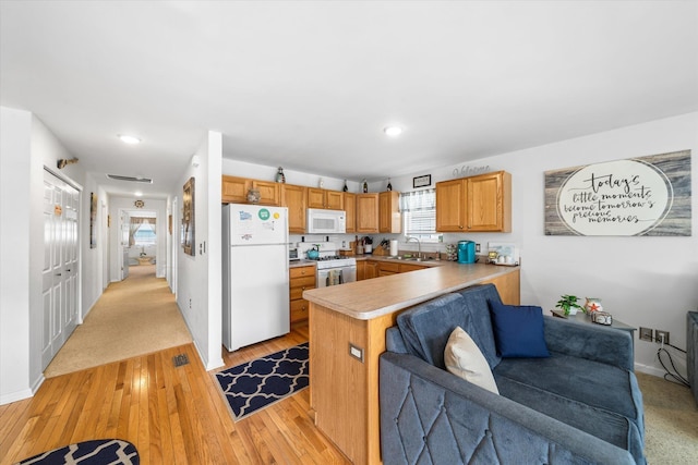 kitchen featuring light countertops, a peninsula, light wood-style floors, white appliances, and a sink