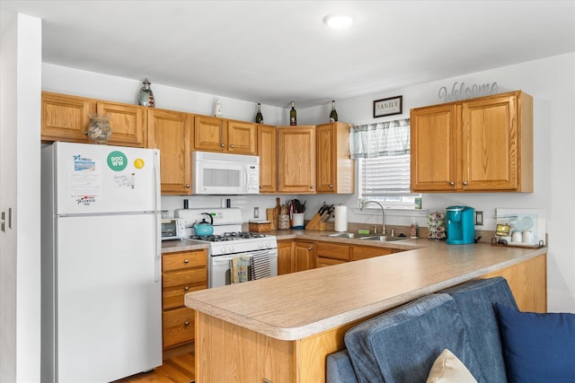 kitchen featuring a sink, a kitchen breakfast bar, white appliances, a peninsula, and light countertops