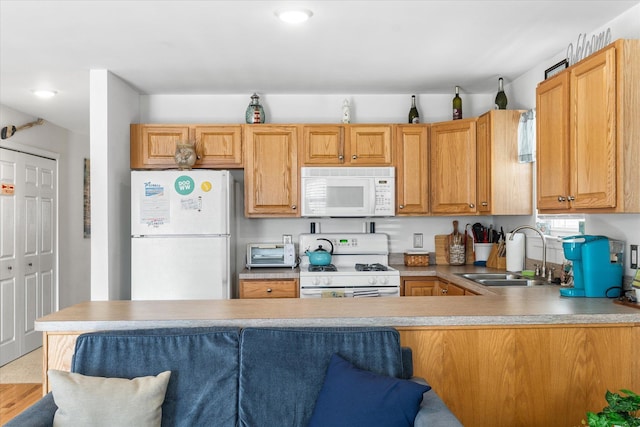 kitchen featuring a kitchen bar, a sink, white appliances, a peninsula, and light countertops