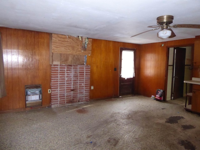 unfurnished living room featuring ceiling fan, heating unit, and wood walls