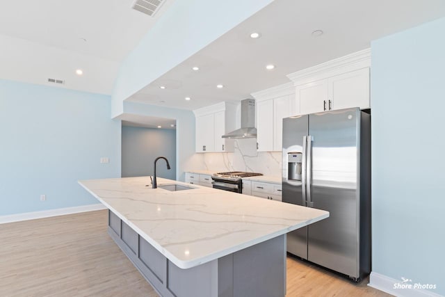 kitchen featuring sink, wall chimney range hood, an island with sink, white cabinets, and appliances with stainless steel finishes