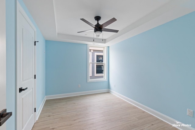 unfurnished room featuring ceiling fan, light wood-type flooring, and a tray ceiling