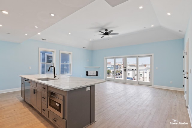 kitchen featuring a center island with sink, sink, ceiling fan, light wood-type flooring, and light stone countertops