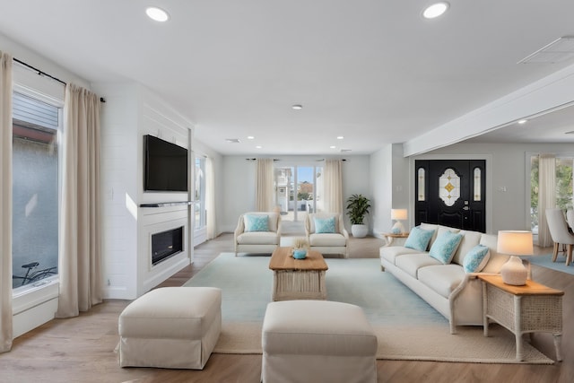 living room with light wood-type flooring, a large fireplace, and a healthy amount of sunlight