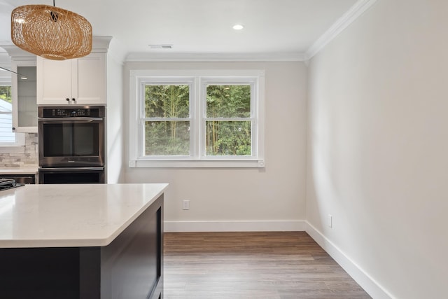 kitchen featuring white cabinets, ornamental molding, tasteful backsplash, light hardwood / wood-style floors, and stainless steel double oven