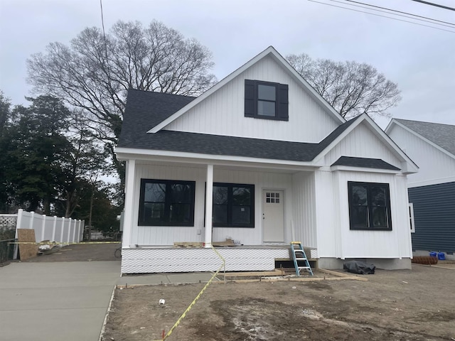 modern inspired farmhouse featuring roof with shingles, covered porch, and fence