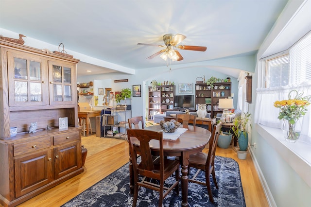 dining space featuring light wood finished floors, baseboards, arched walkways, and a ceiling fan