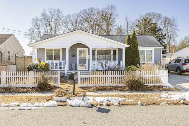 bungalow-style home with a porch, roof with shingles, driveway, and a fenced front yard