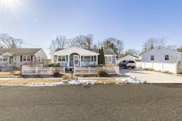 bungalow featuring covered porch, driveway, and a fenced front yard