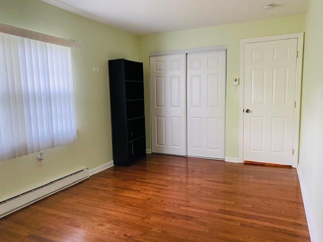 unfurnished bedroom with wood-type flooring, baseboard heating, and a closet