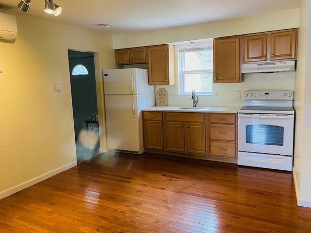 kitchen with white appliances, sink, dark wood-type flooring, and an AC wall unit