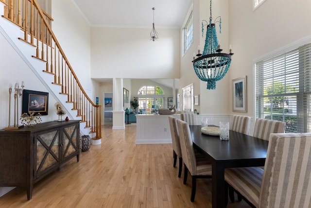 dining space with crown molding, light hardwood / wood-style flooring, a towering ceiling, and a chandelier