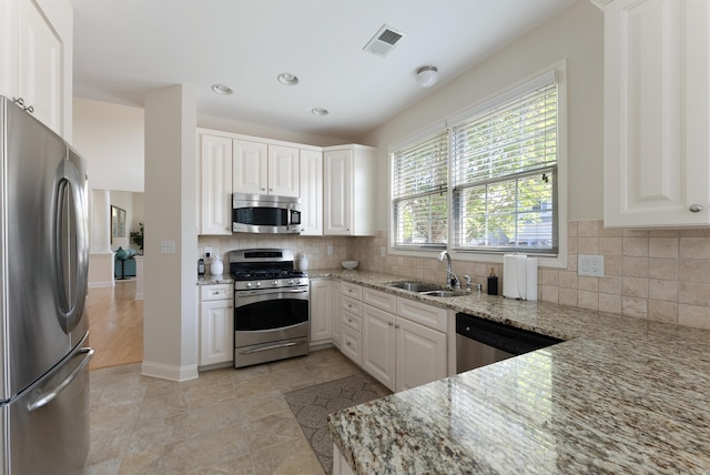 kitchen with light stone countertops, appliances with stainless steel finishes, white cabinetry, and sink