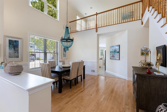 dining area featuring a towering ceiling, light hardwood / wood-style flooring, and an inviting chandelier