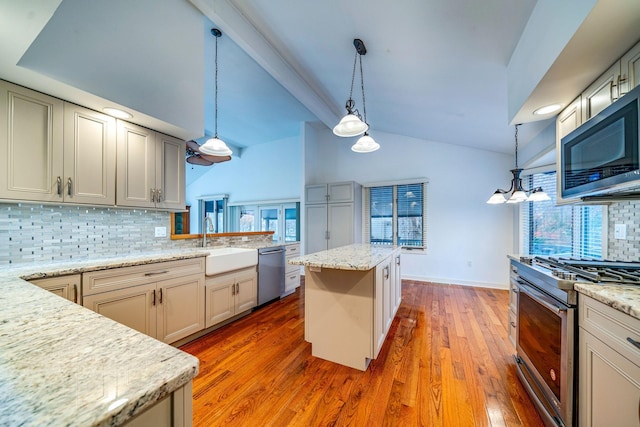 kitchen featuring light stone counters, stainless steel appliances, a kitchen island, a sink, and decorative light fixtures