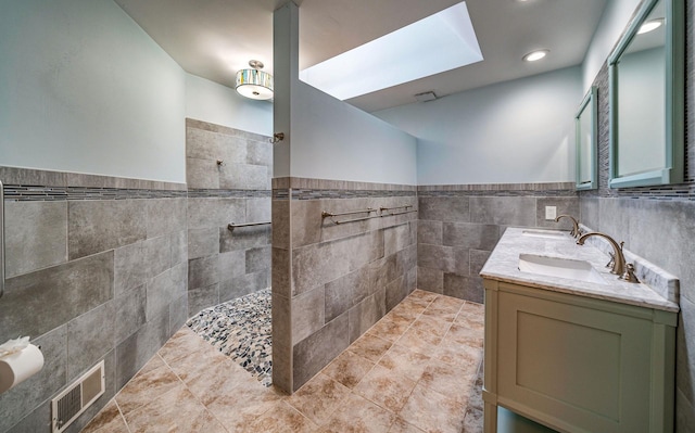 bathroom featuring tile walls, double vanity, visible vents, a sink, and walk in shower