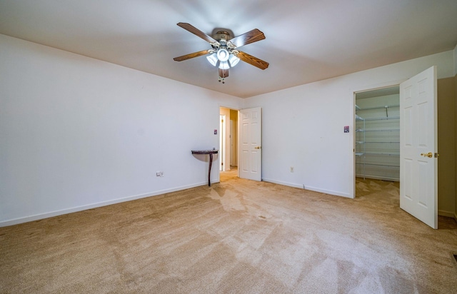 unfurnished bedroom with light carpet, a spacious closet, baseboards, and a ceiling fan