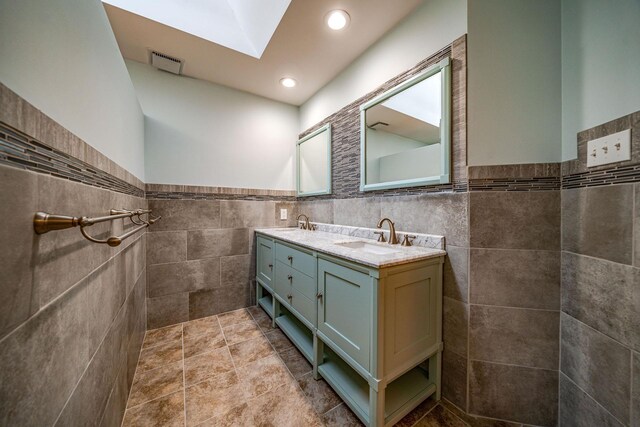 full bath with double vanity, a sink, visible vents, and tile walls