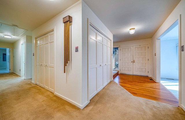 corridor featuring light carpet, attic access, and baseboards