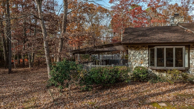 rear view of house featuring stone siding, roof with shingles, and a chimney