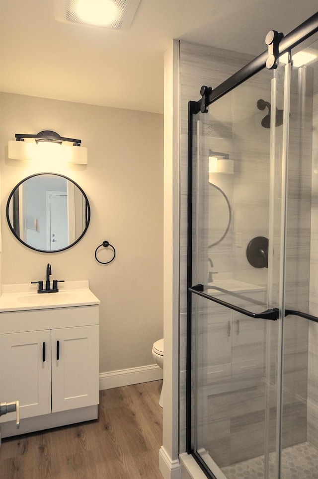 bathroom with a stall shower, vanity, toilet, and wood finished floors