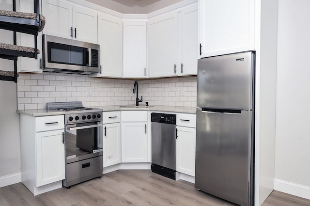 kitchen featuring appliances with stainless steel finishes, a sink, light stone countertops, light wood-type flooring, and backsplash