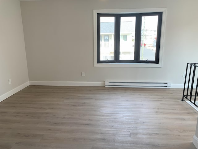 spare room with baseboards, a baseboard heating unit, and wood finished floors