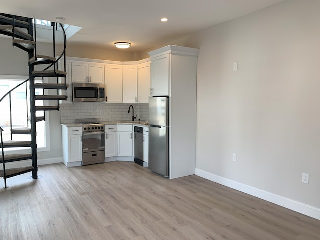 kitchen with stainless steel appliances, tasteful backsplash, light countertops, white cabinetry, and a sink