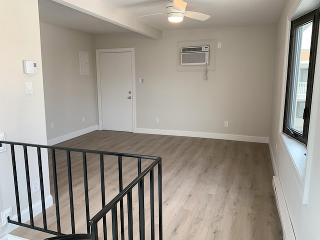 empty room featuring light wood finished floors, baseboards, baseboard heating, and an AC wall unit