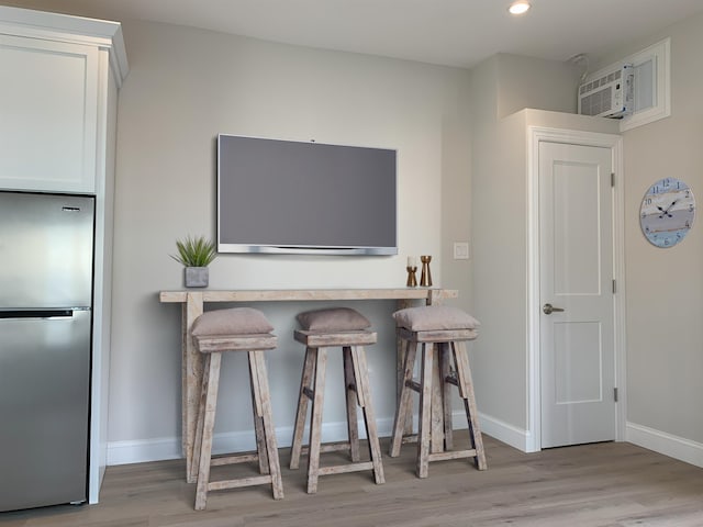 kitchen with stainless steel fridge, light wood-style flooring, a kitchen bar, white cabinetry, and a wall mounted AC