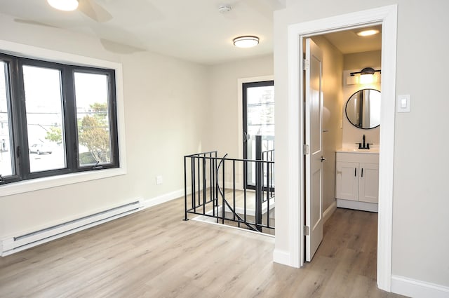 hallway with plenty of natural light, a baseboard heating unit, a sink, and an upstairs landing